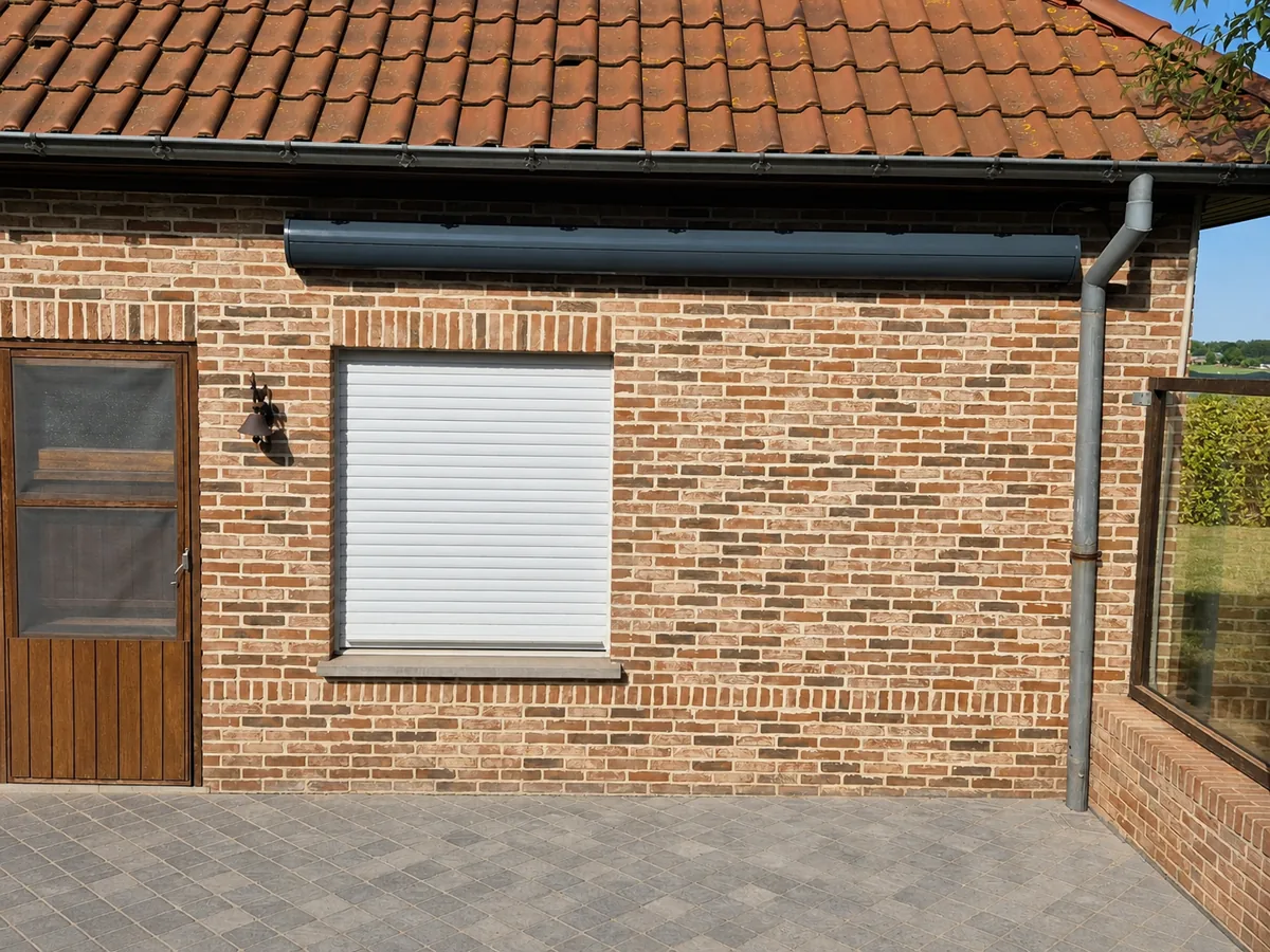Cassette sombre d'un auvent à bras repliables contre une façade en brique rurale